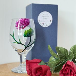 Stemmed lager glass with a hand painted thistle, gift box and decorative flower beside it