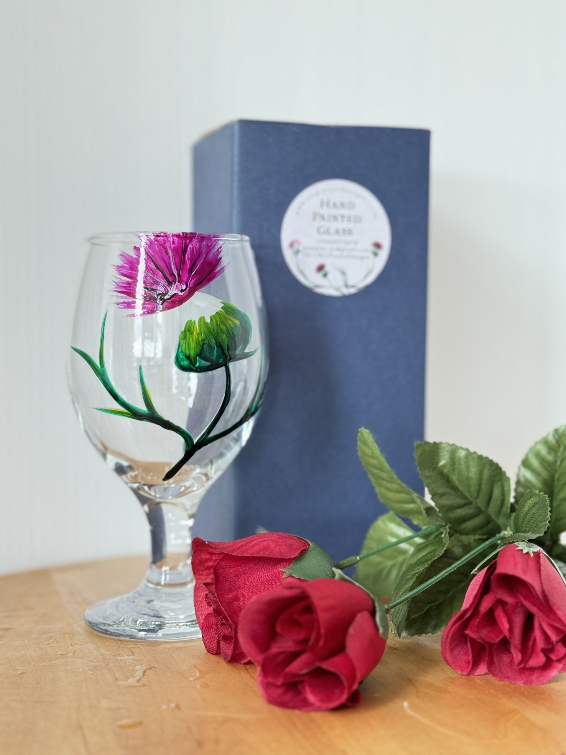 Stemmed lager glass with a hand painted thistle, gift box and decorative flower beside it